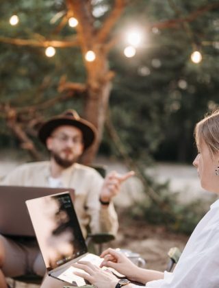 Two digital nomads sitting on the bitch with their laptops in their laps.