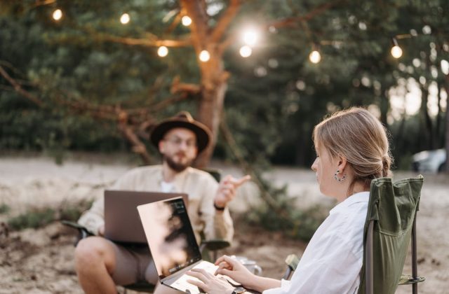 Two digital nomads sitting on the bitch with their laptops in their laps.