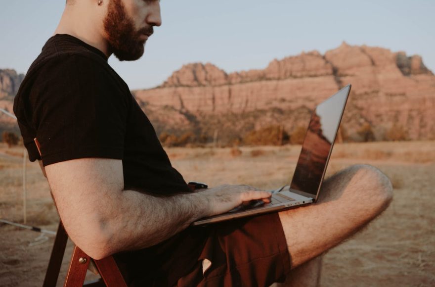 Remote worker using laptop outdoors in Sedona desert landscape with red rock formations — working from anywhere as a digital nomad in 2026